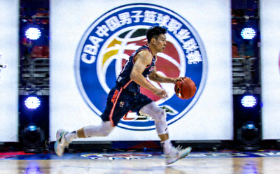 CBA中国男子篮球职业联赛比赛画面 - 国内球员运球突破，背景是鲜明的球队Logo