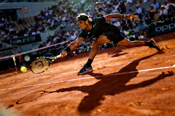 网球大满贯决赛现场 - 球员在红土场上奋力救球，阳光照射下身影被拉长，画面极具张力